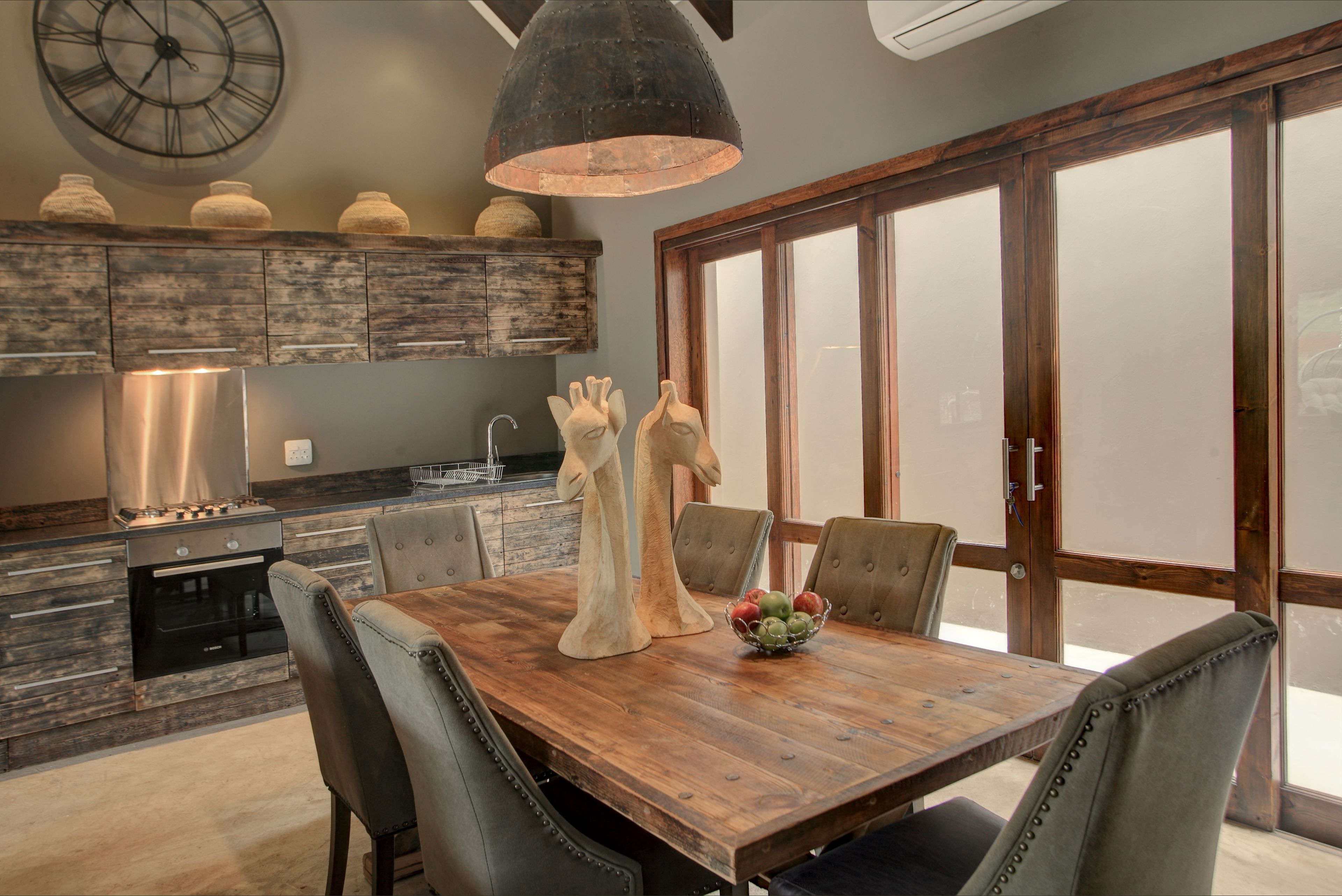 A modern kitchen with a wooden dining table, chairs, and a large window.