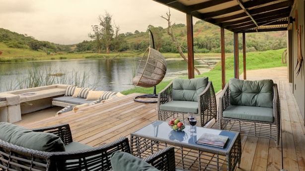 A wooden deck with wicker furniture, a hanging chair, and a table with fruit and a glass of wine.