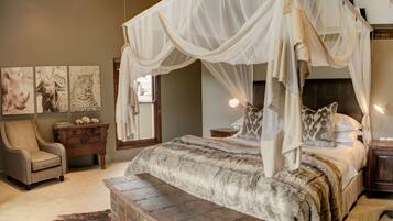 A four-poster canopy bed with a fur-like bedspread, a wooden chest, a chair, and artwork on the wall.