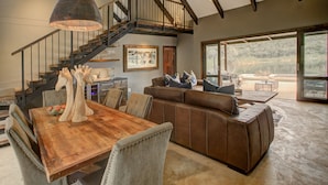 A spacious living area with a wooden dining table, leather sofa, and a staircase leading to an upper level.