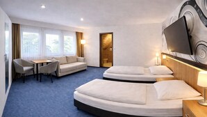 A hotel room with a sofa, two beds, a TV, and a desk.
