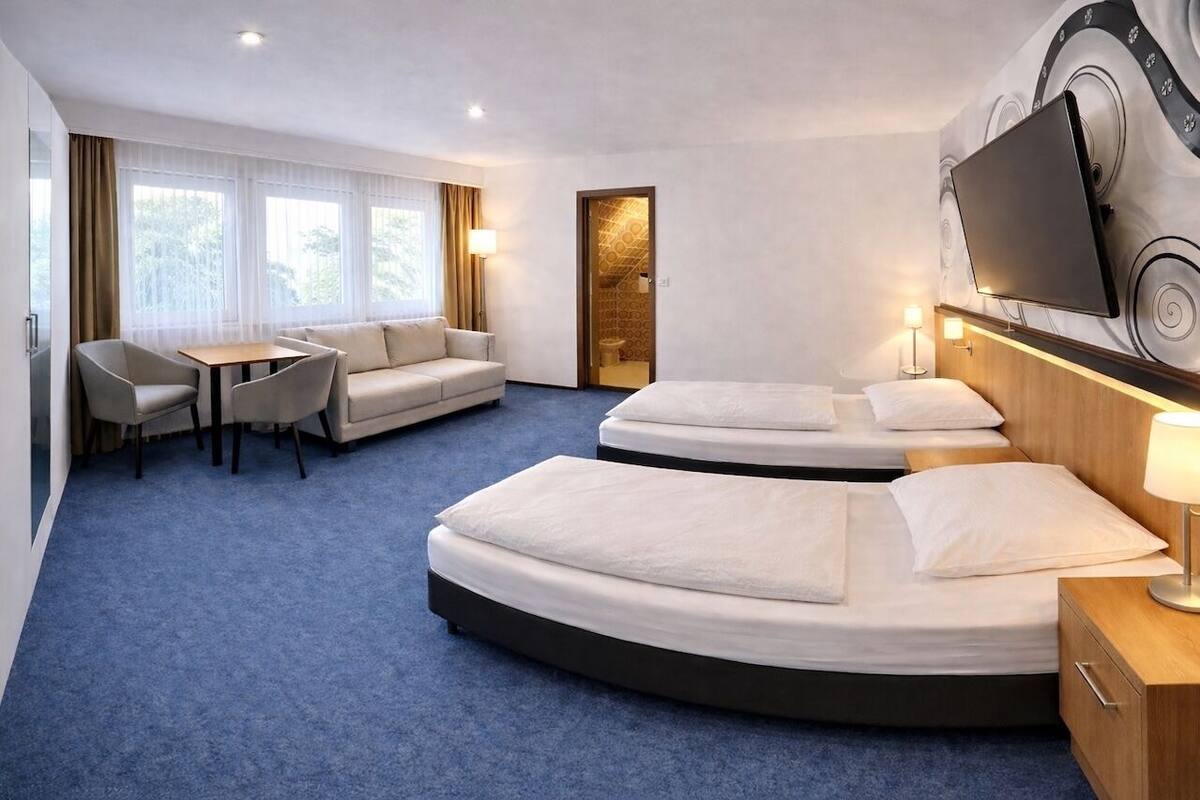 A hotel room with a sofa, two beds, a TV, and a desk.