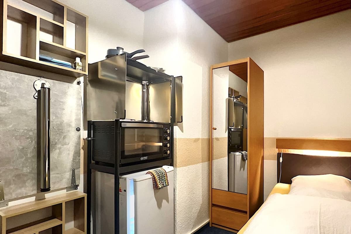 A compact room with a bed, a built-in microwave, a refrigerator, and a mirror.