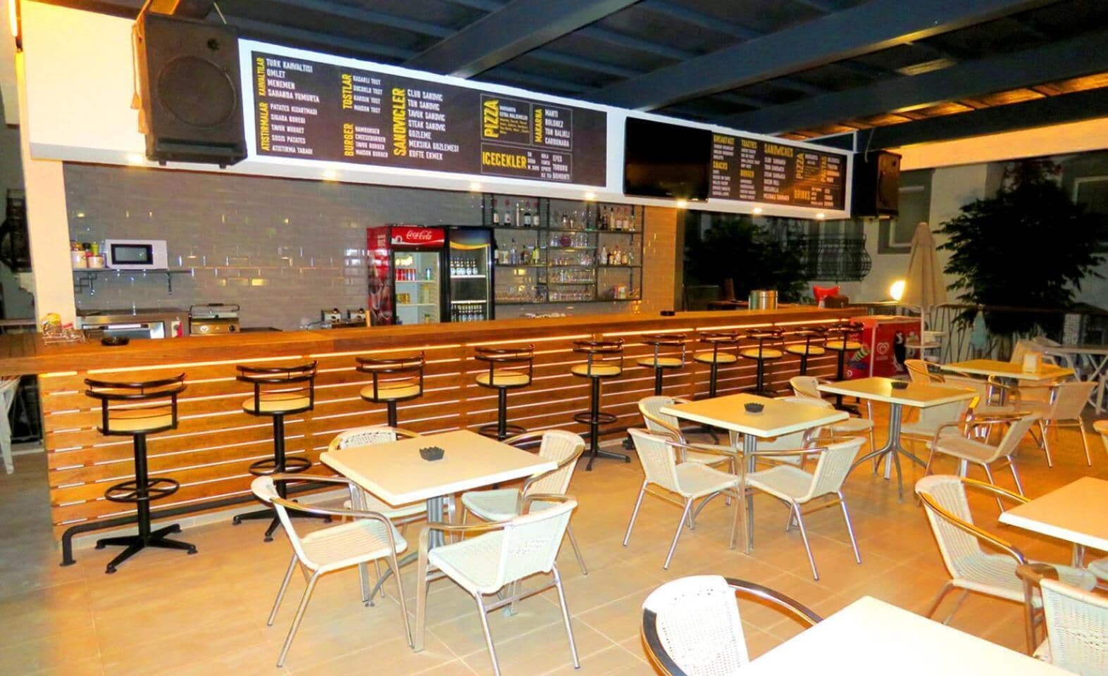 A restaurant with a bar area, multiple seating options including tables and chairs, and a menu board above the bar.