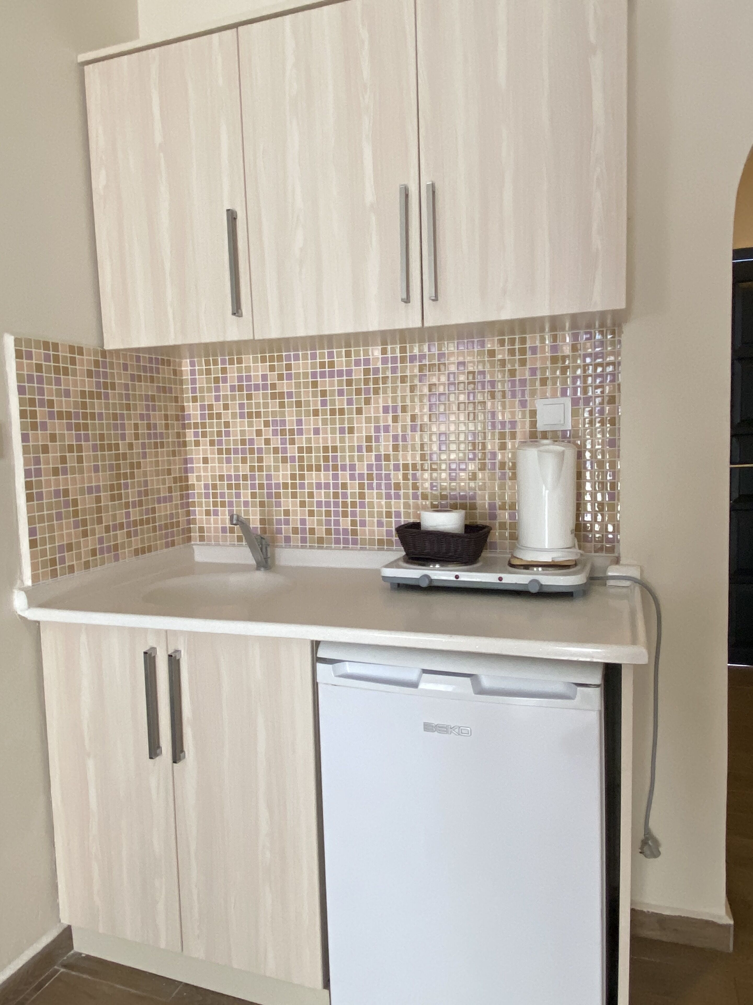 Cocina compacta con muebles blancos, salpicadero de azulejos y lavavajillas pequeño.