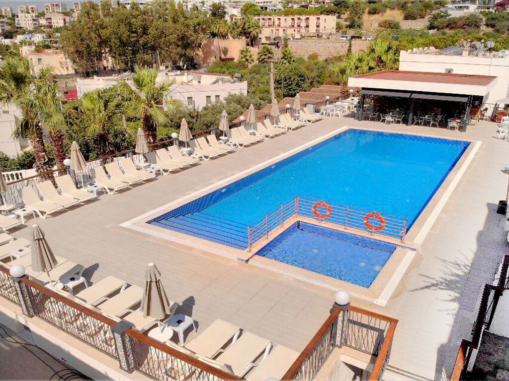 A rooftop swimming pool with lounge chairs and umbrellas, surrounded by buildings and trees.