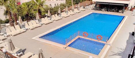Una piscina en la azotea con sillones y sombrillas, rodeada de edificios y árboles.