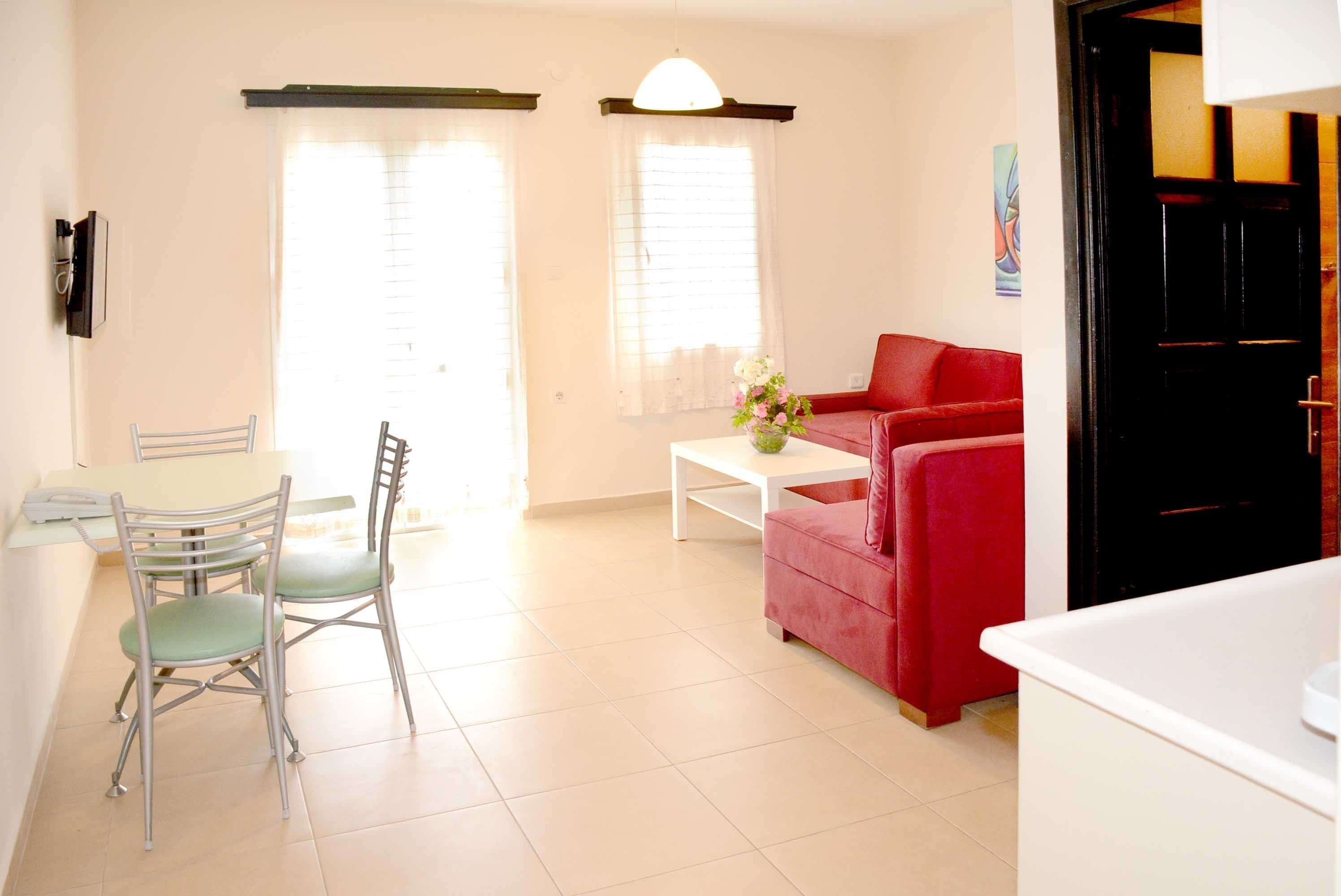 Una sala de estar con un sofá rojo, una mesa de comedor con sillas y una mesa de centro blanca con flores.