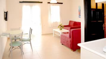 Una sala de estar con un sofá rojo, una mesa de comedor con sillas y una mesa de centro blanca con flores.