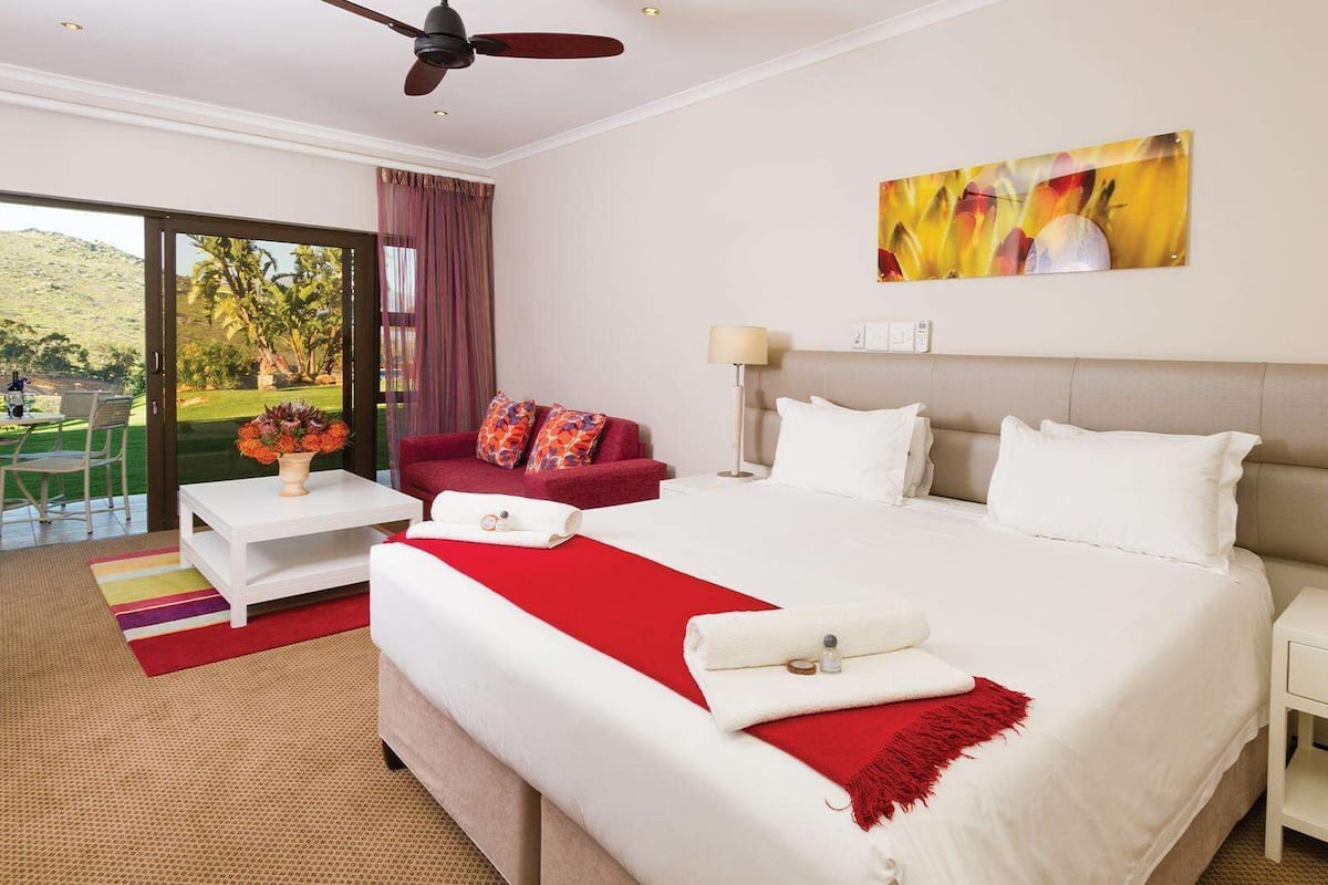 A hotel room with a large bed, a red sofa, a small table with a vase of flowers, and a painting on the wall.