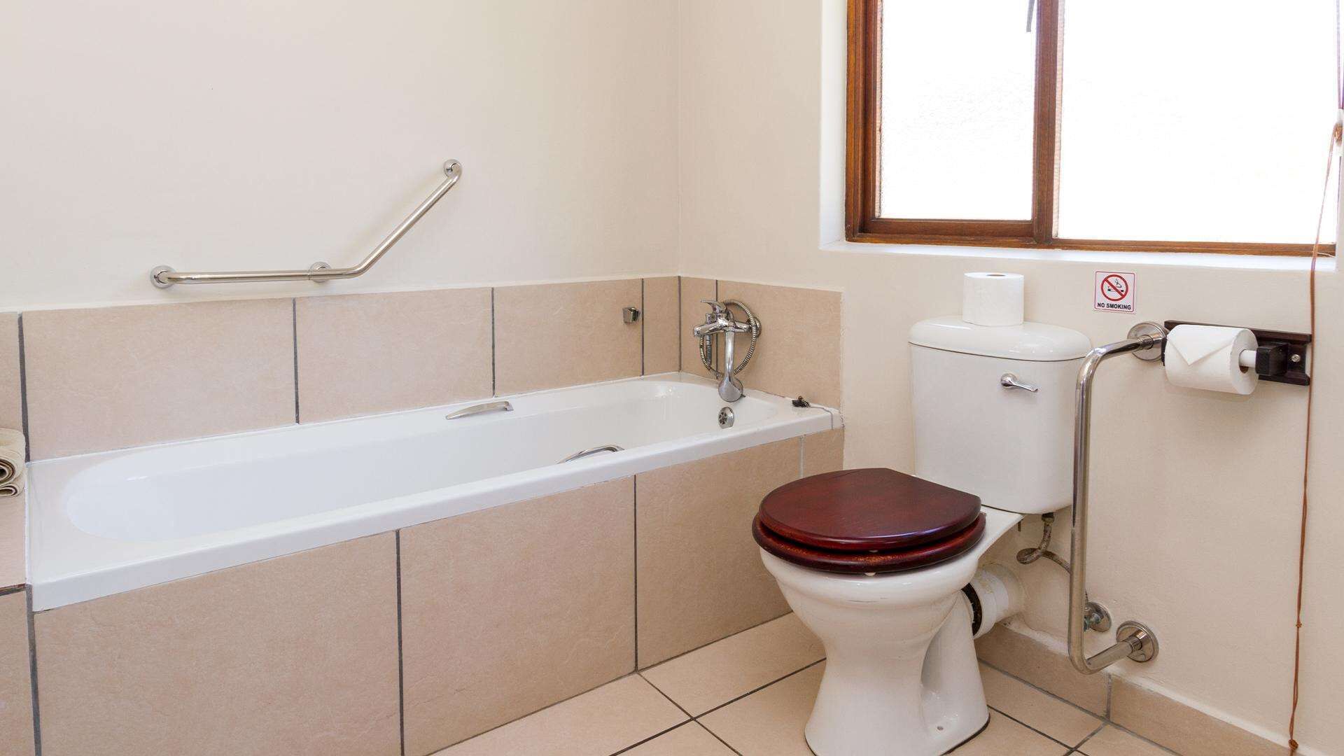 Een badkamer met een wit bad, een houten toilet en een rookvrij bord aan de muur.
