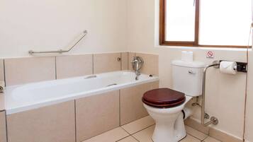 Een badkamer met een wit bad, een houten toilet en een rookvrij bord aan de muur.