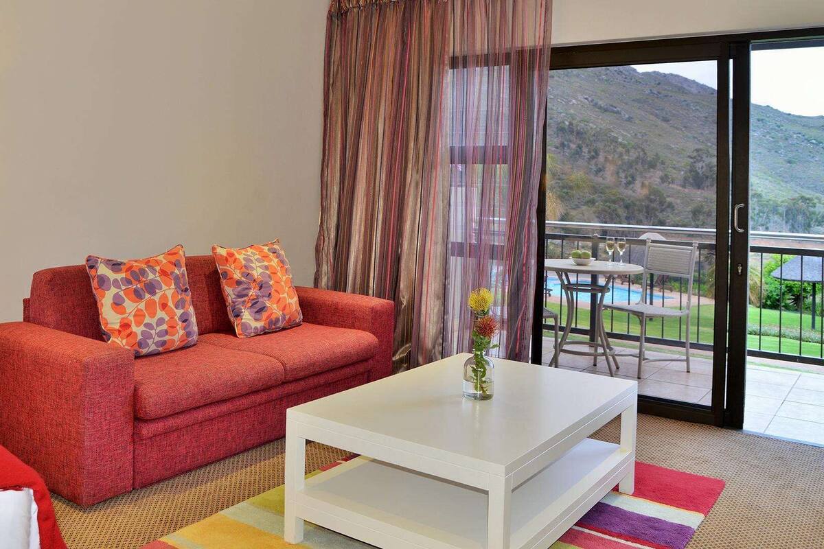 A room with a red sofa, white coffee table, and a view of a mountainous landscape through a sliding door.