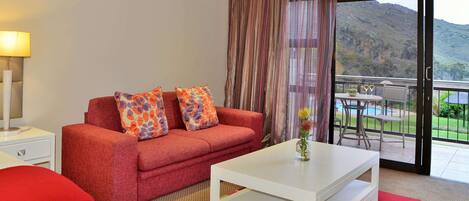A room with a red sofa, white coffee table, and a view of a mountainous landscape through a sliding door.