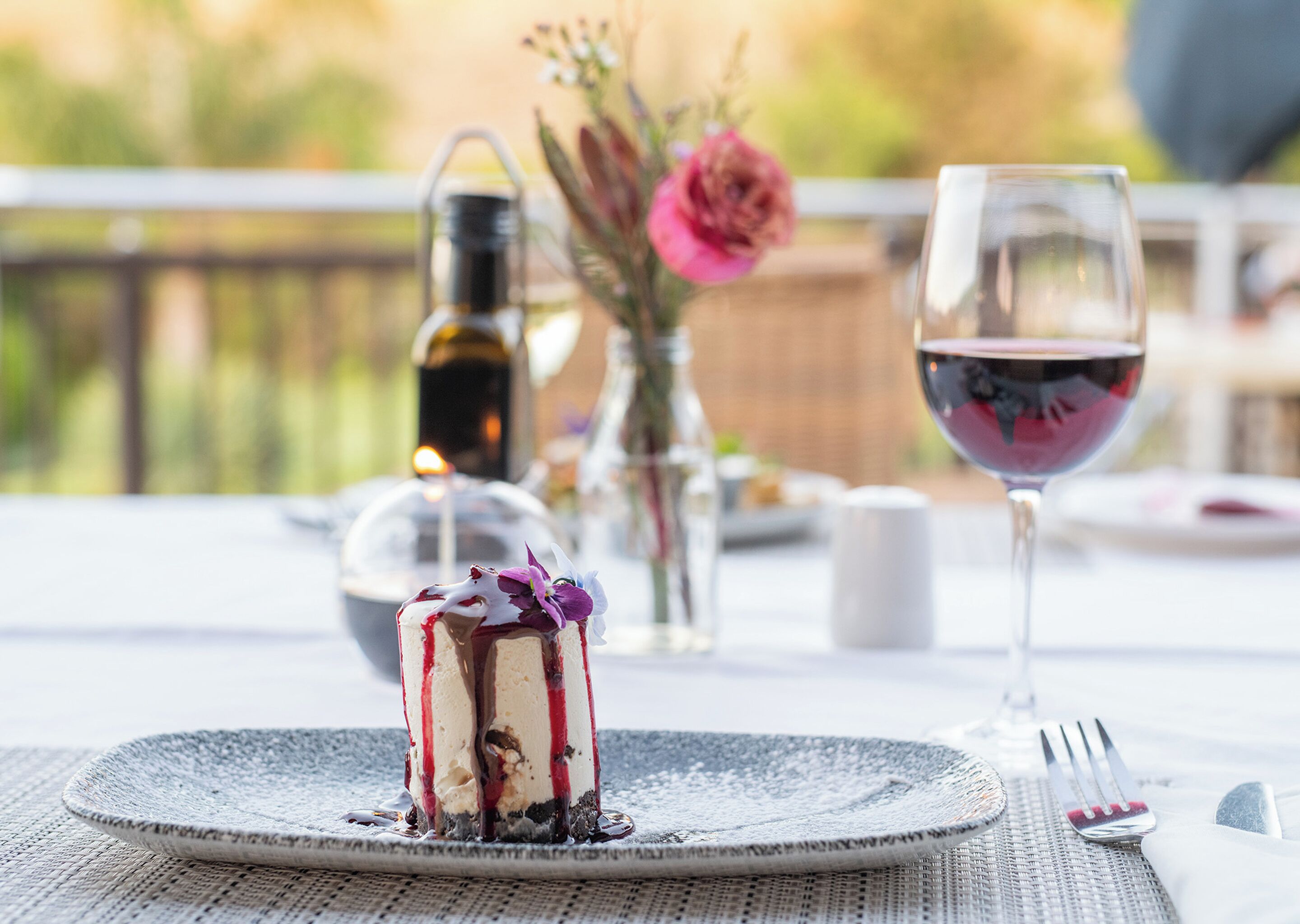 A dessert on a plate with a glass of red wine and a bottle of wine on a table outdoors.