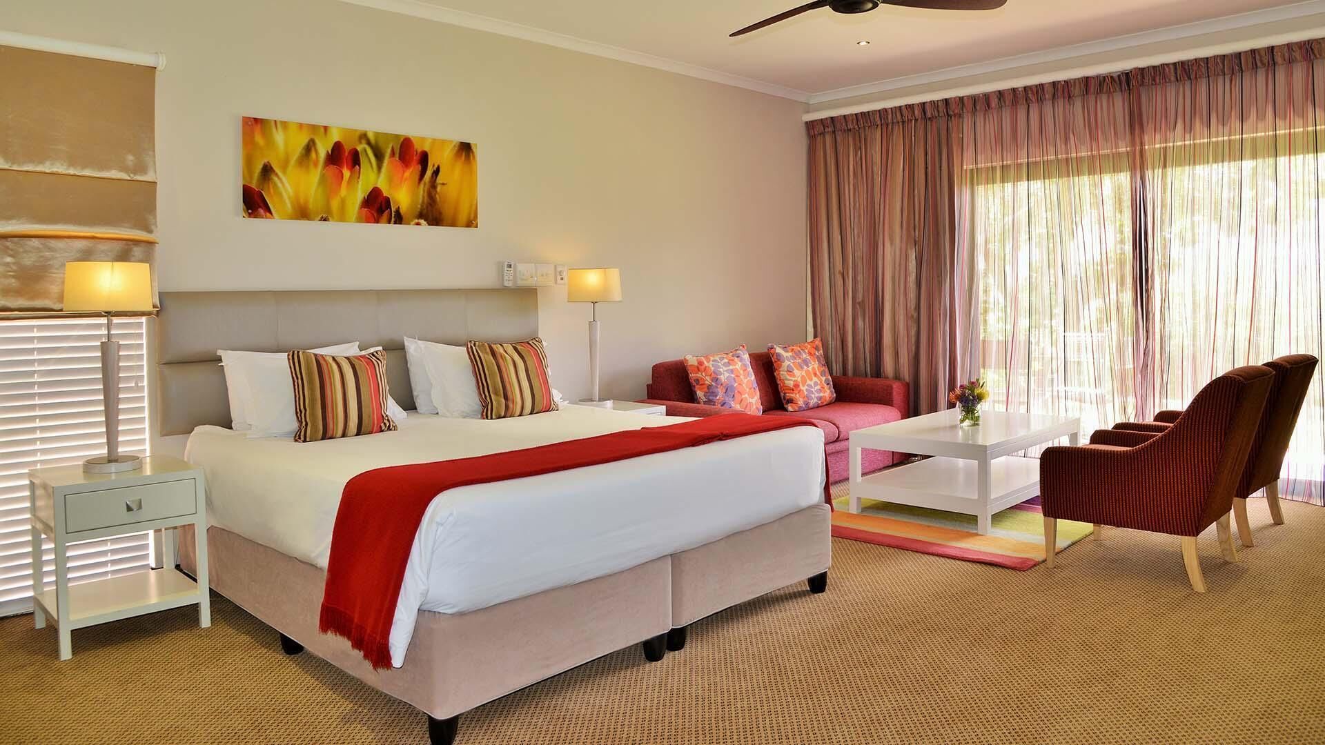 A hotel room with a bed, a sofa, a chair, a coffee table, and a painting on the wall.