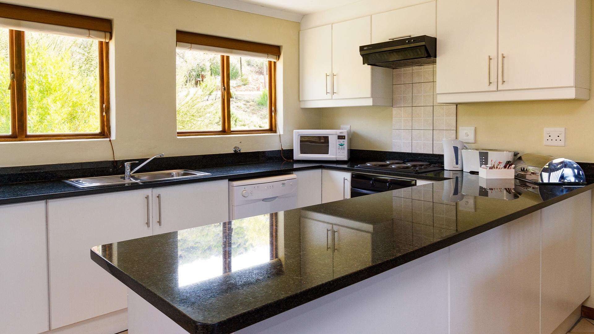 A modern kitchen with white cabinets, a black countertop, a microwave, a stove, and a sink.