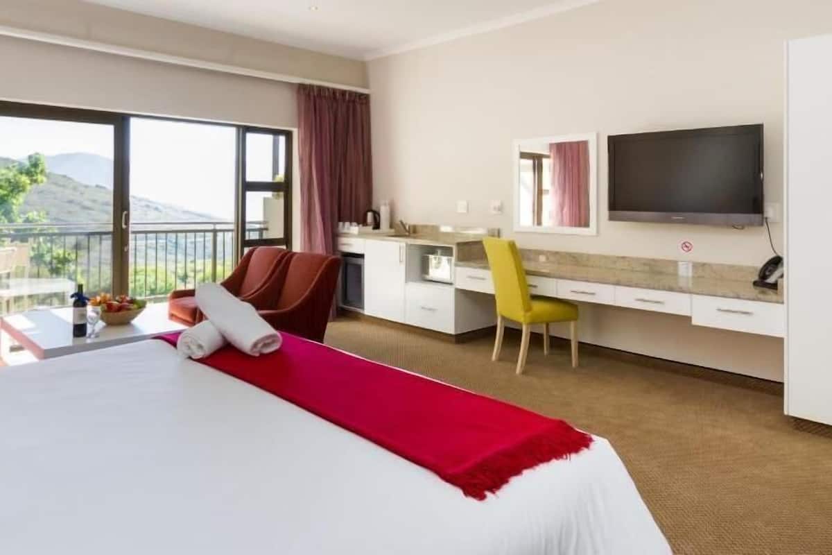 A hotel room with a bed, a desk, a chair, a TV, and a balcony with a view.