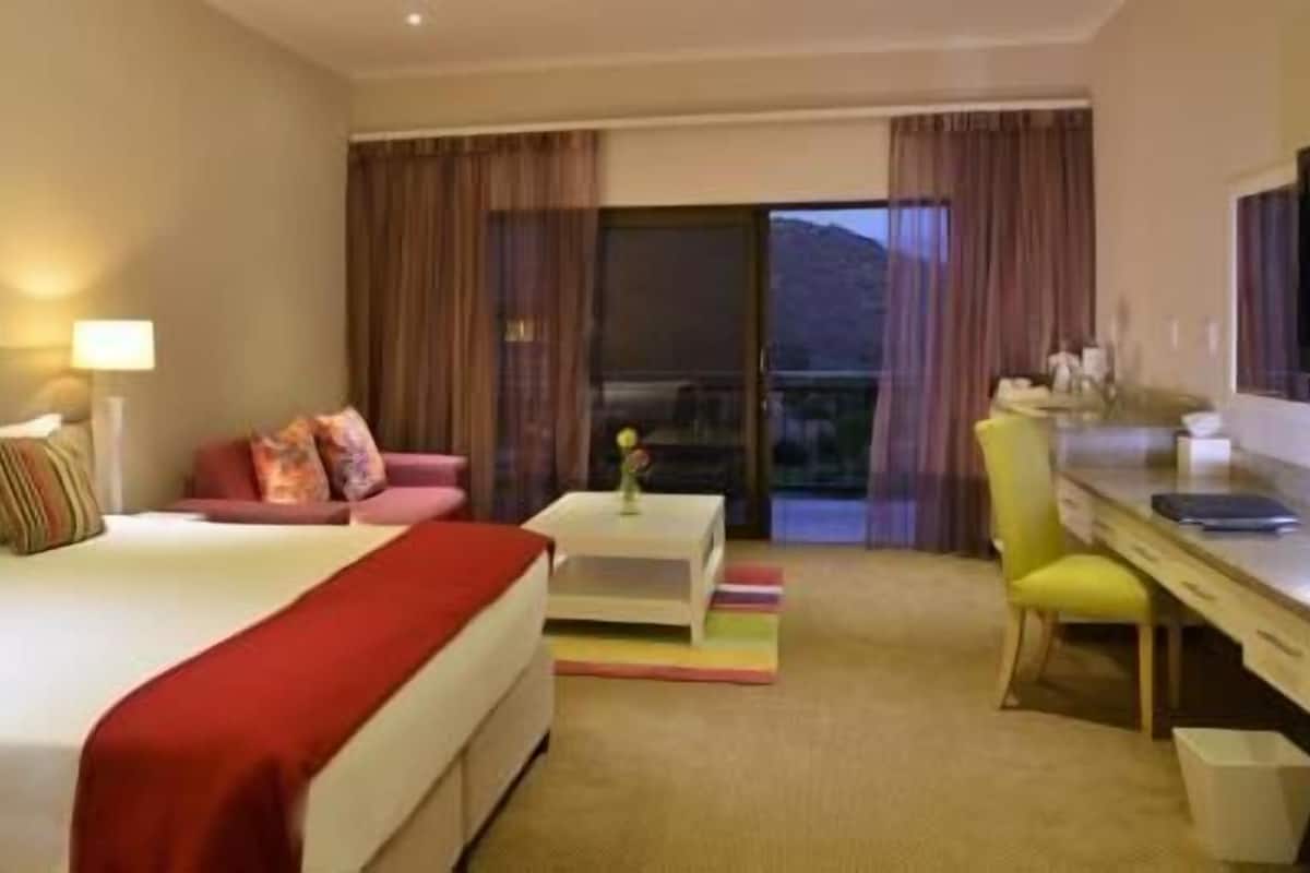 A hotel room with a bed, a desk, a chair, a small table, and a view of the outdoors.