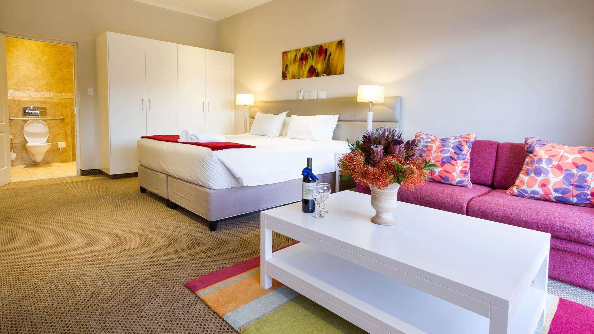 A hotel room with a bed, a white coffee table, a sofa, and a bathroom with a toilet and shower.