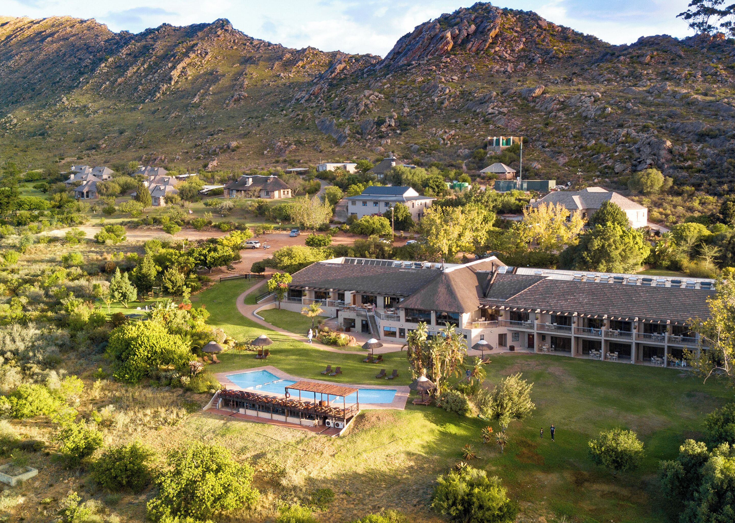 A resort with a pool, multiple buildings, and a mountainous backdrop.