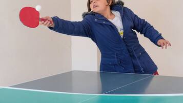 A child playing table tennis in a room with a green table and white walls.