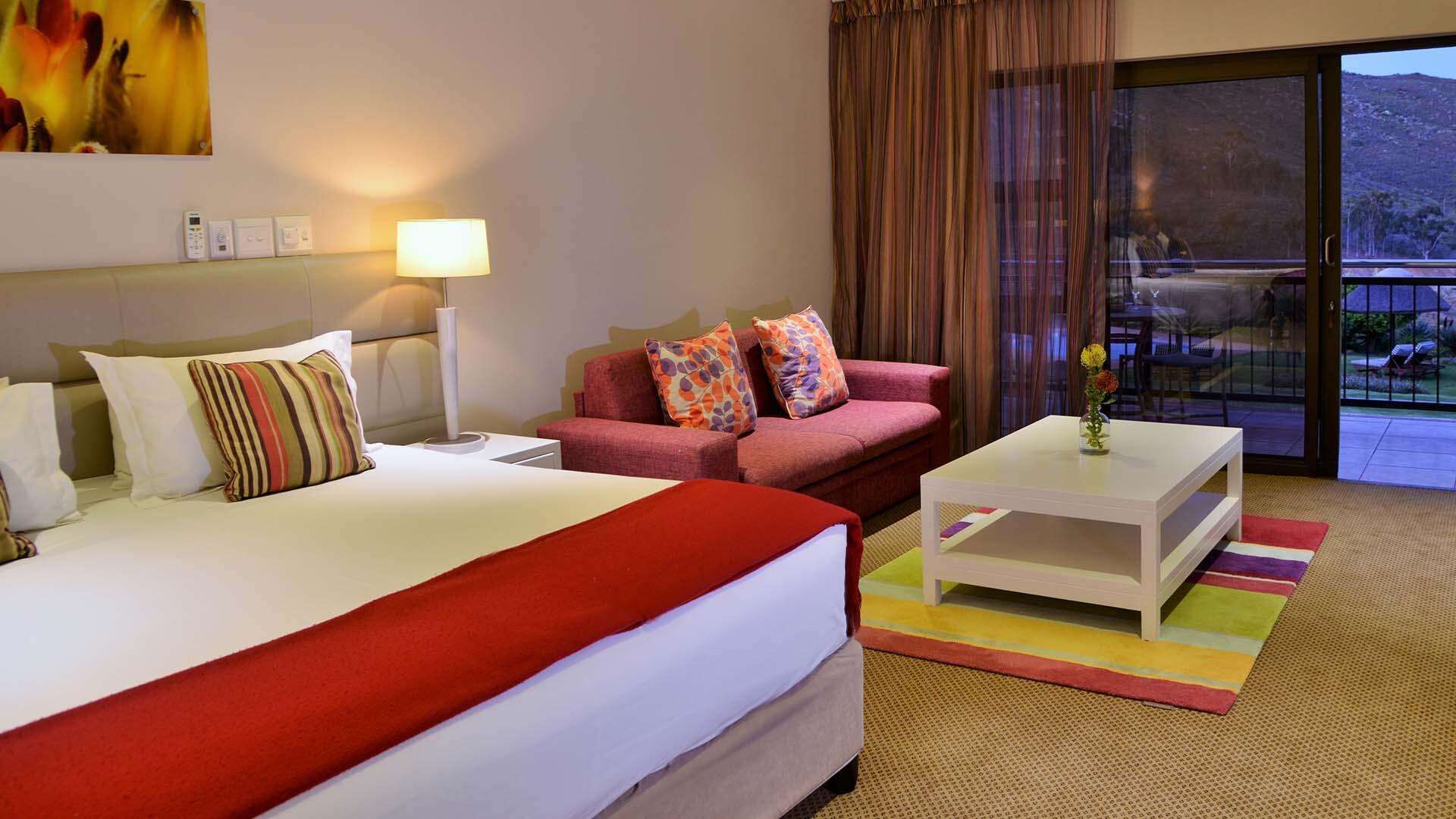 A hotel room with a bed, a sofa, a coffee table, and a view of the outdoors through a glass door.