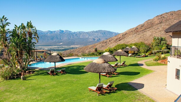 A poolside area with lounge chairs and umbrellas, a swimming pool, and a mountainous backdrop. - Piekenierskloof Mountain Resort by Dream Resorts (Bergrivier)