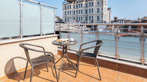 A balcony with two wicker chairs and a small table, overlooking a river with buildings in the background. - Mint Residence Taksim (Istanbul)