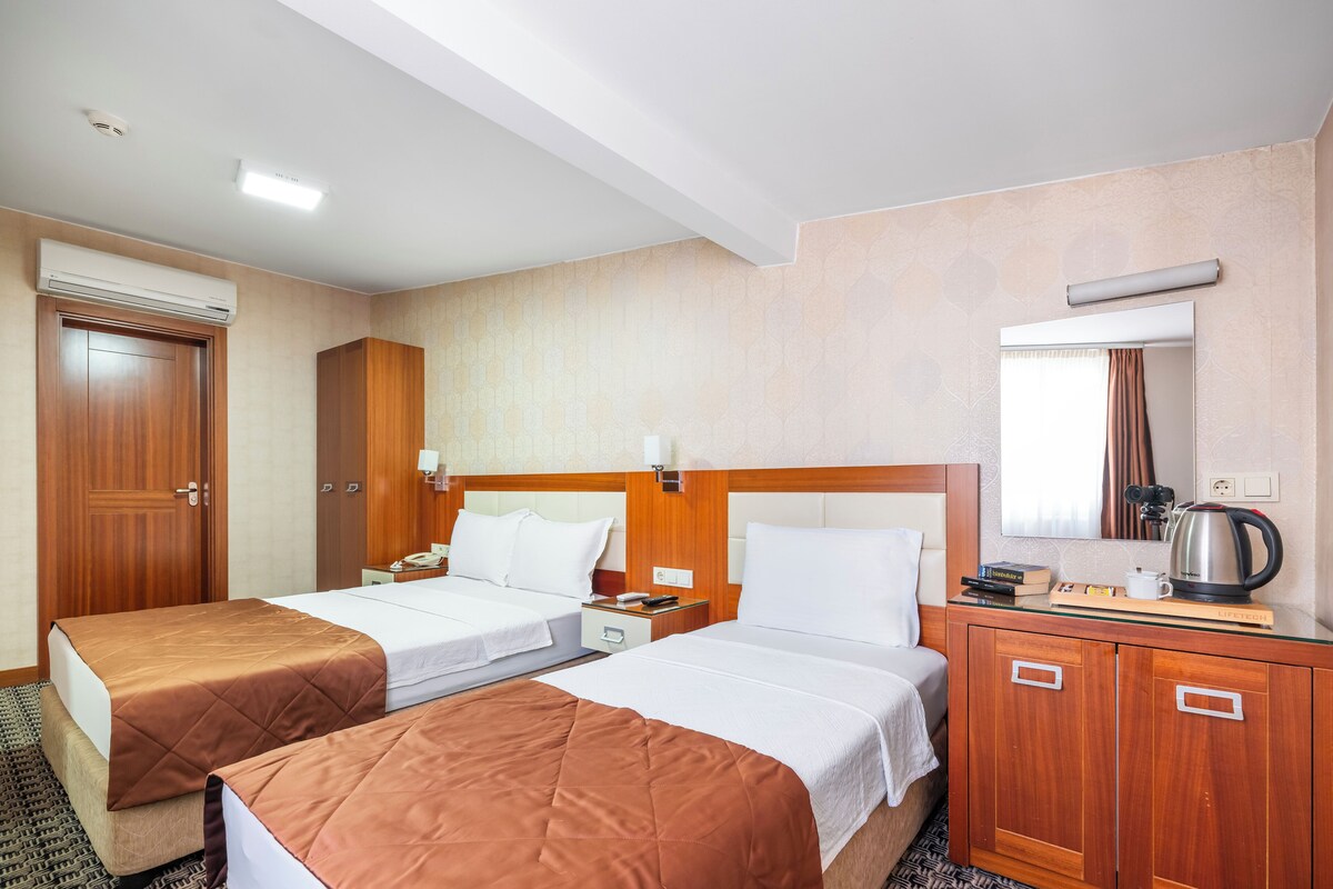 A hotel room with two beds, a wooden wardrobe, a mirror, a coffee maker, and a telephone.