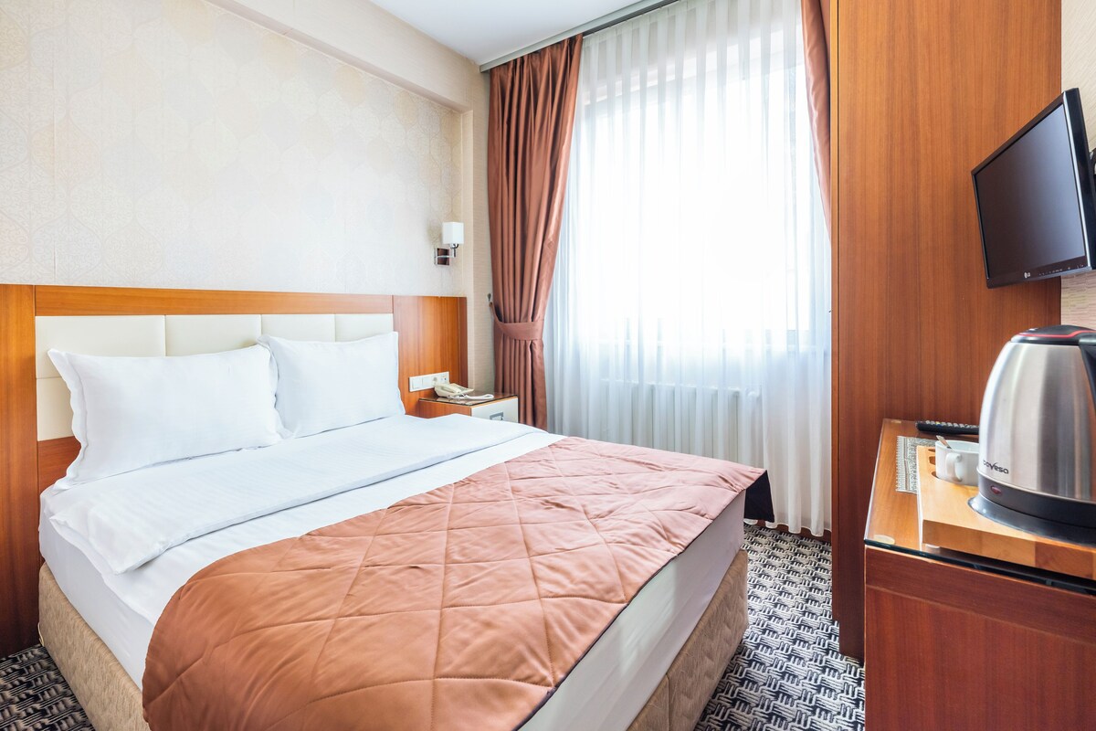 A hotel room with a bed, a nightstand, a television, and a coffee maker.
