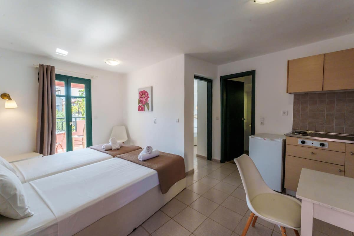 A hotel room with two beds, a small kitchenette, a dining table, and a chair.
