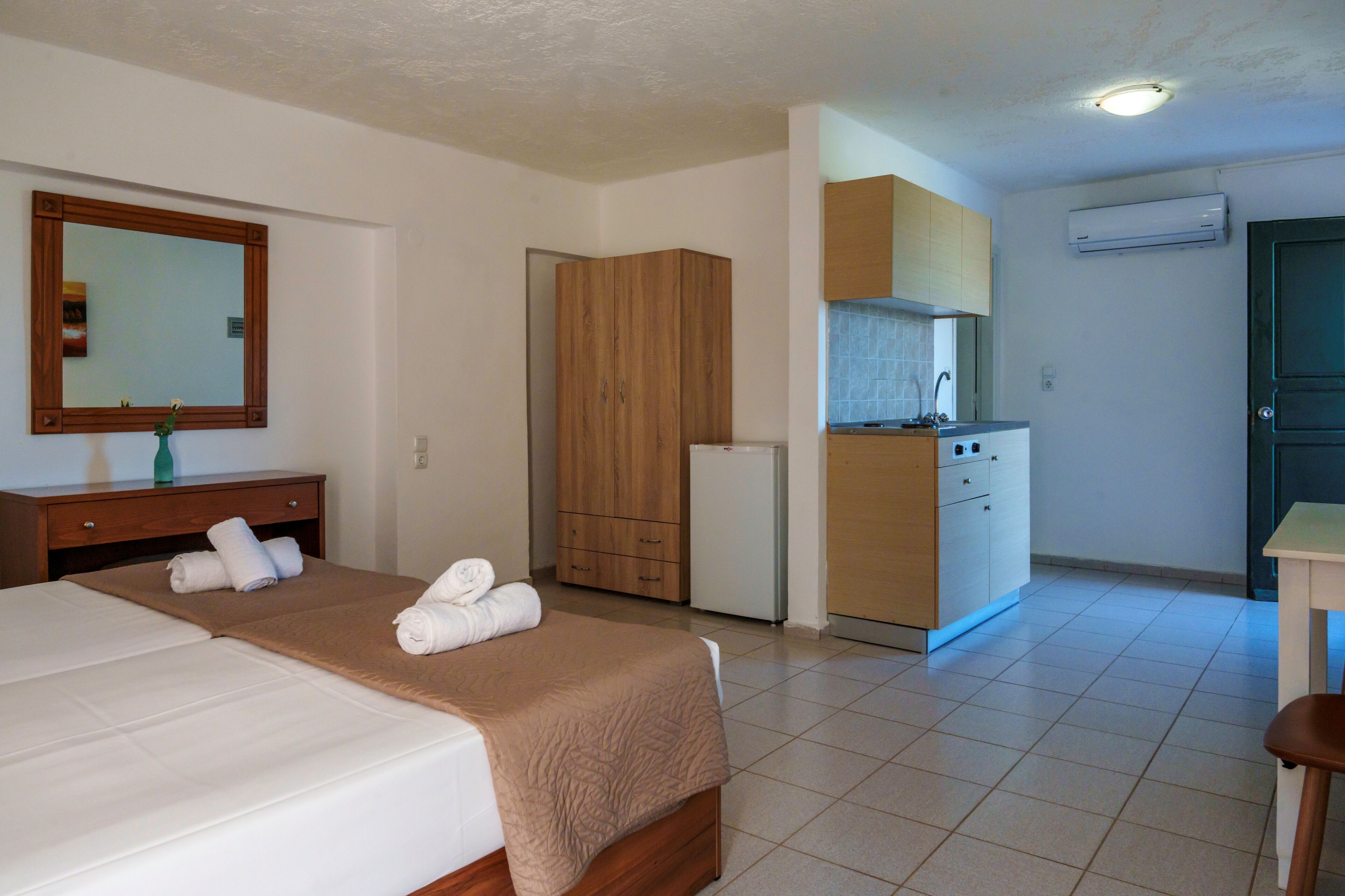 A hotel room with a bed, a wooden wardrobe, a small kitchenette, and a bathroom.