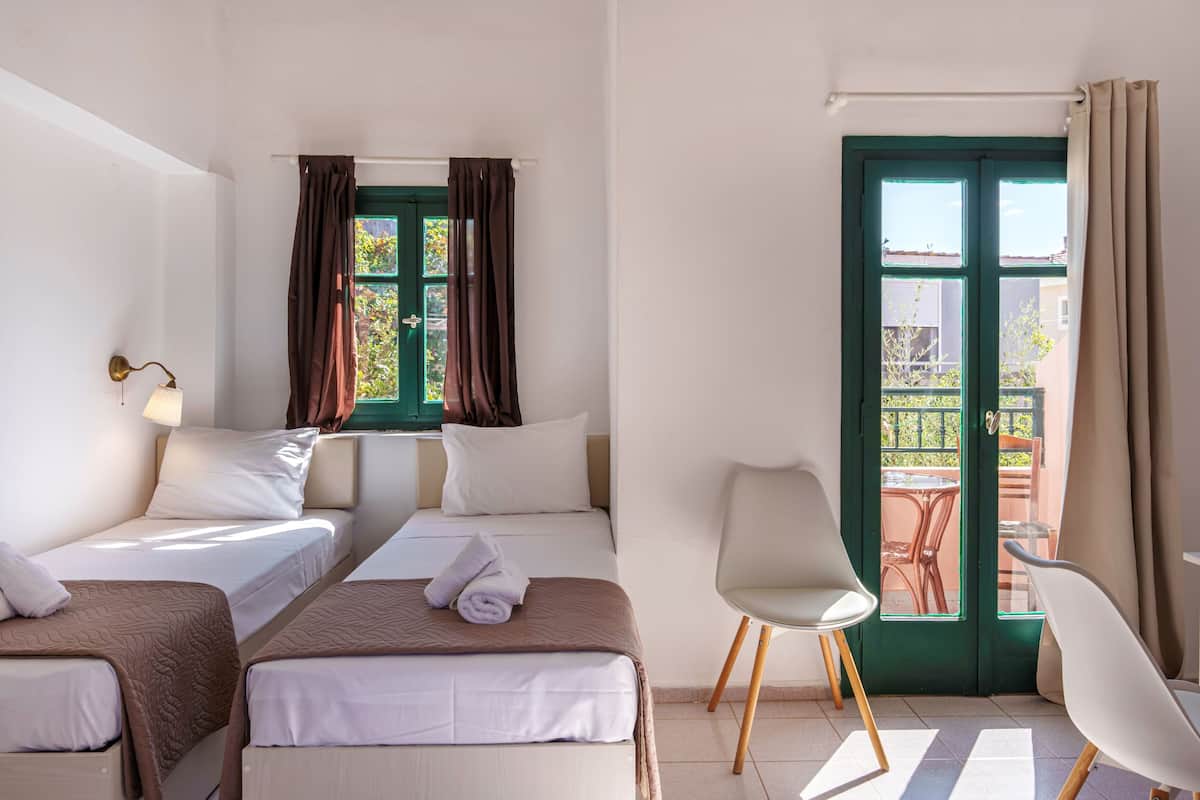A hotel room with two beds, a balcony with a table and chairs, and a view of the outside.