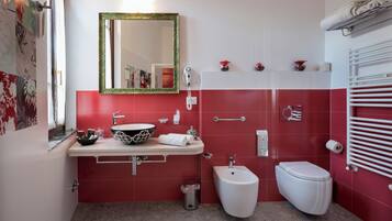 A bathroom with a red and white color scheme, a sink with a bowl, a bidet, a toilet, a mirror with a green frame, and a towel rack.
