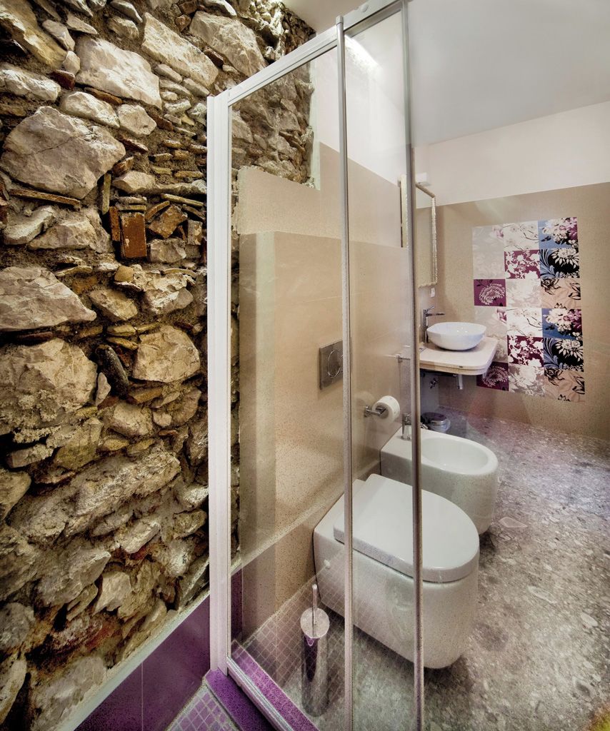 A bathroom with a stone wall, a glass shower enclosure, and two toilets.