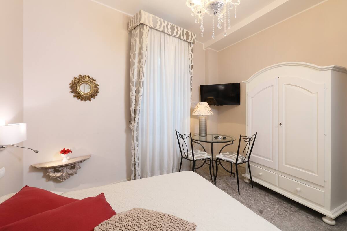 Ein Hotelzimmer mit einem Bett, einem kleinen Tisch mit Stühlen, einem Fernseher, einem Kleiderschrank und einem dekorativen Spiegel.