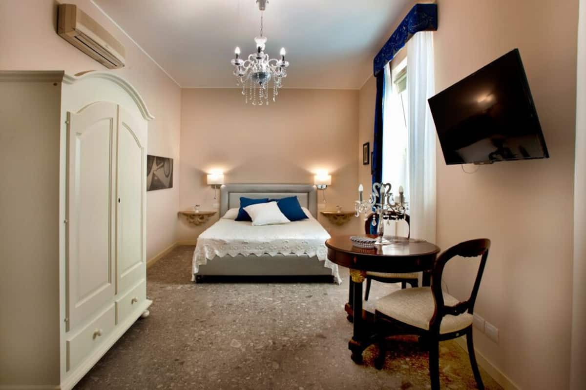 Ein Schlafzimmer mit einem Bett, Nachttischen, einer Chandelieber, einem Fernseher und einem Sessel.