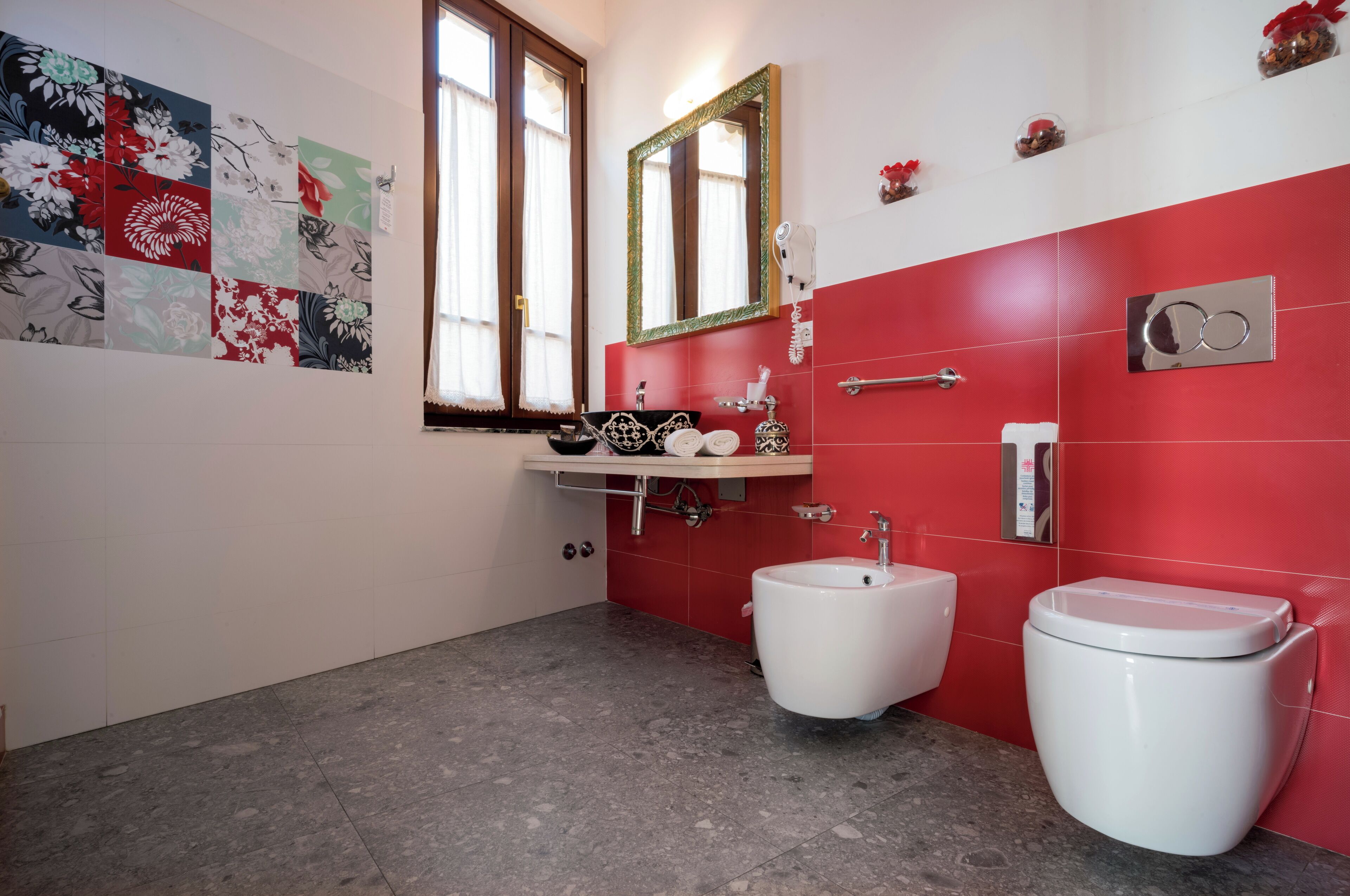 Un baño con pared de azulejos rojos, inodoro blanco, bidé y lavabo con espejo superior.