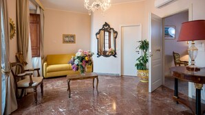 Ein Zimmer mit Marmorboden, einem gelben Sofa, einem Holztisch mit Blumenarrangements, einer Kristallleuchtre und einer roten Lampe.