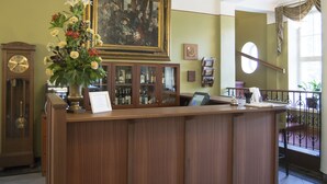 A reception area with a wooden reception desk, a clock, a framed painting, and a display of liquor bottles. - Hotel Hirvihaaran Kartano (Maentsaelae)
