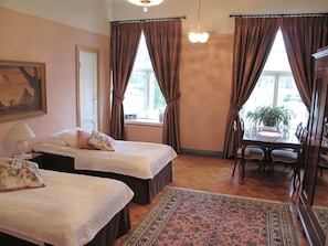 A hotel room with two beds, a dining table, and a chandelier. - Hotel Hirvihaaran Kartano (Maentsaelae)