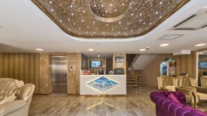 A hotel reception area with a modern design, featuring a reception desk, a staircase, and plush seating. - Grand Pamir Hotel (Istanbul)