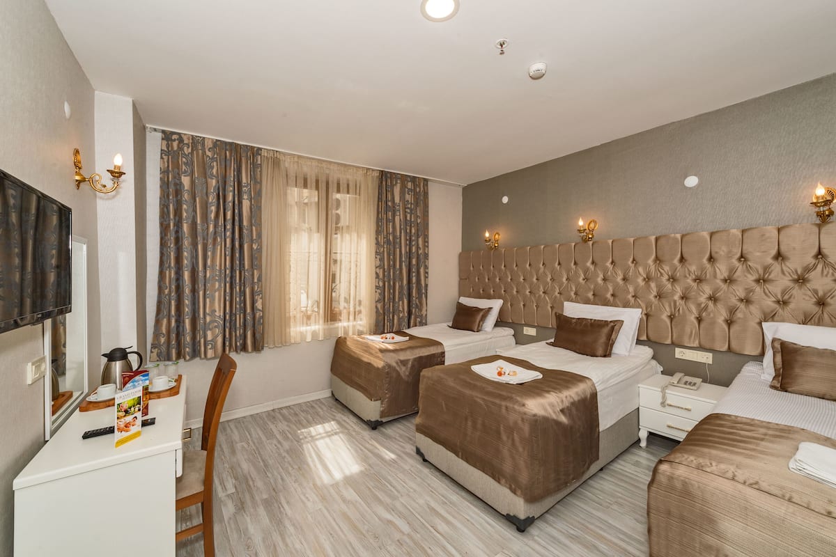 A hotel room with two beds, a desk, a chair, a TV, and a window with curtains.