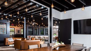 A modern dining area with a wooden table, cushioned seating, pendant lighting, and a large window offering a view of the outdoors. - Hotel Nyack, a JdV by Hyatt Hotel (Nyack)