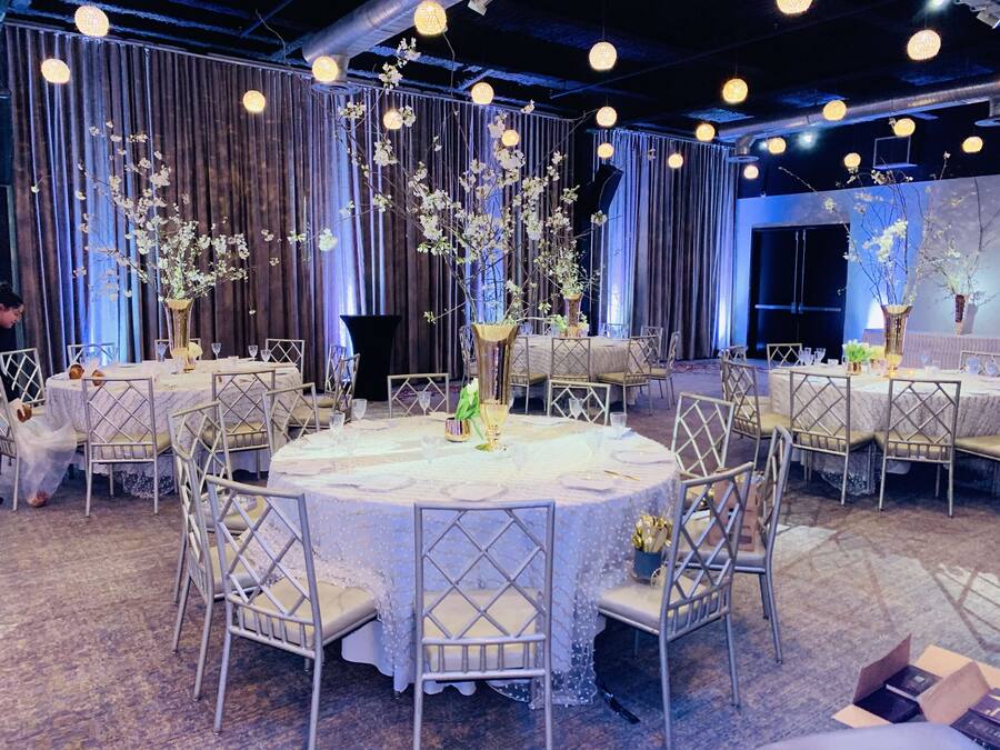 Un salón de banquetes con mesas redondas, sillas blancas y centros de mesa con flores.