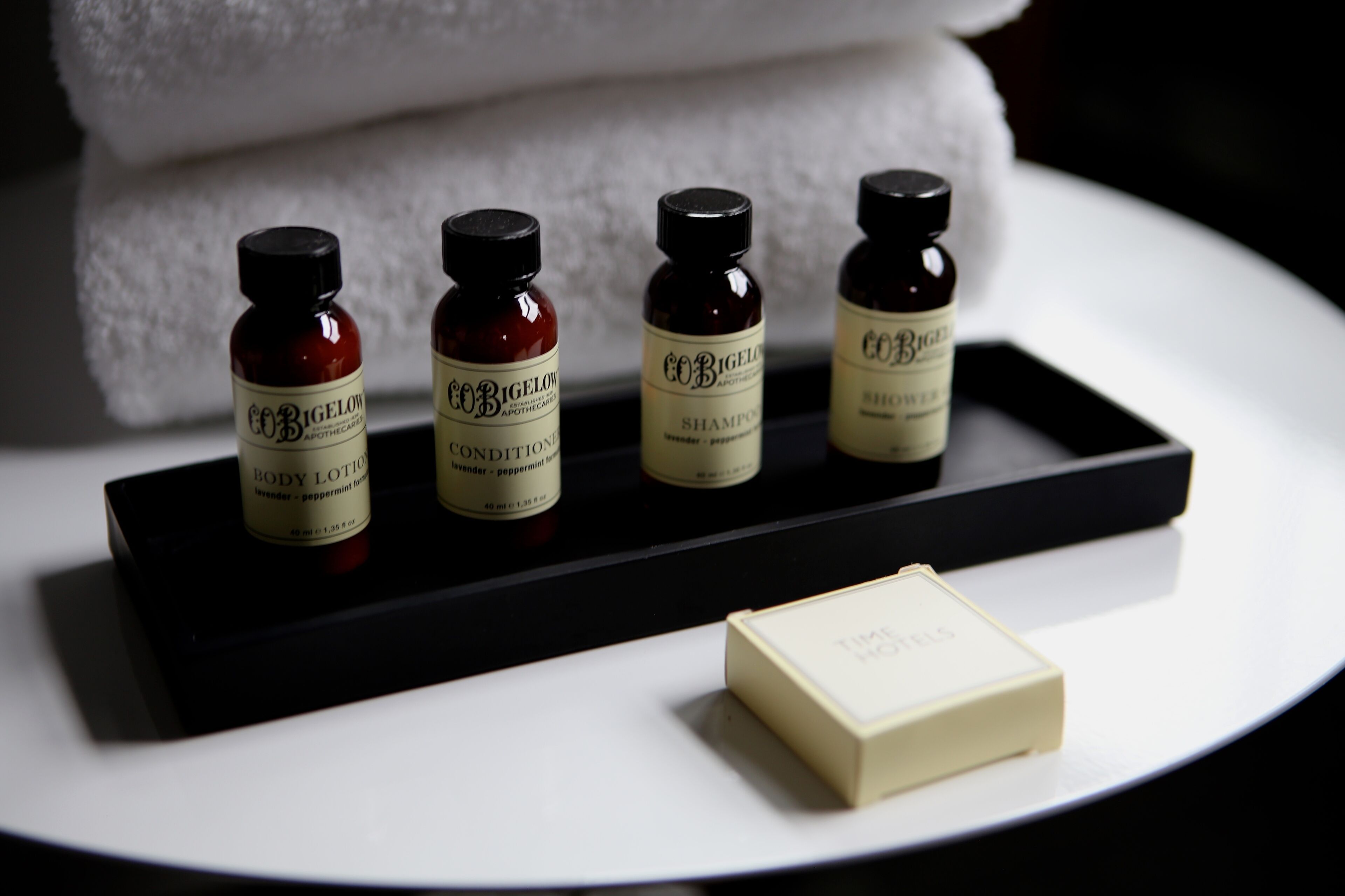 Four bottles of CoBigelow body lotion and conditioner on a black tray, with a bar of soap beside them.