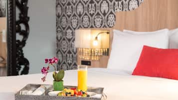 A neatly made bed with a tray of breakfast items including fruits, a glass of orange juice, and a small orchid.