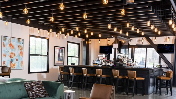 A modern bar area with a bar counter, multiple stools, and a seating area with a sofa and chairs. - Hotel Nyack, a JdV by Hyatt Hotel (Nyack)