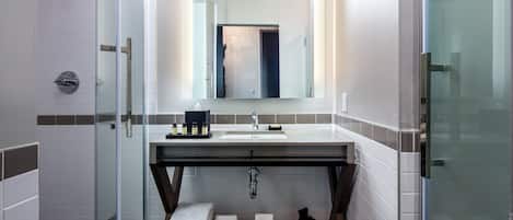 Un baño moderno con ducha de vidrio, lavamanos con espejo y toallas ordenadas en un estante de madera.